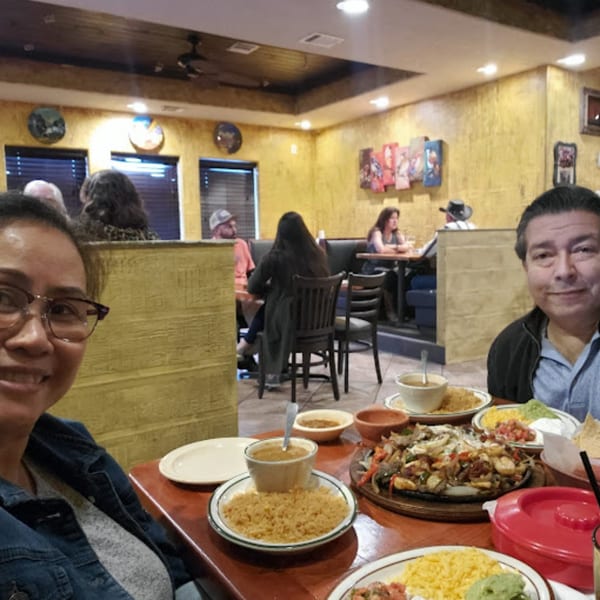Two people smiling at a table with fajitas, rice, and other Mexican dishes at Pueblo Viejo.