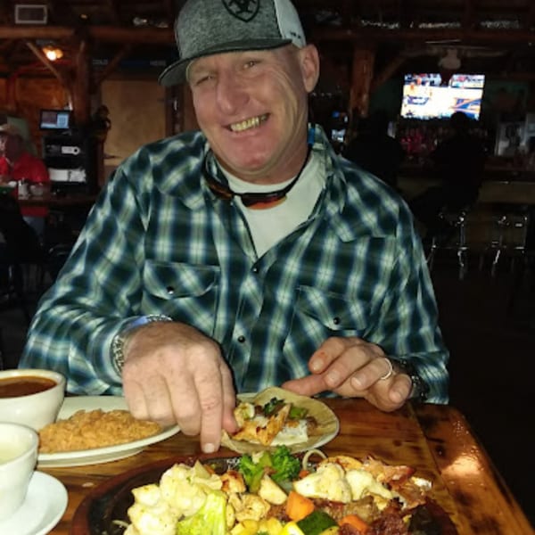 A smiling man in a plaid shirt and cap enjoys a taco and fajitas at Pueblo Viejo Mexican Restaurant.