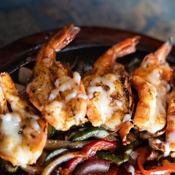 Sizzling shrimp fajitas with melted cheese, bell peppers, and onions in a hot skillet.