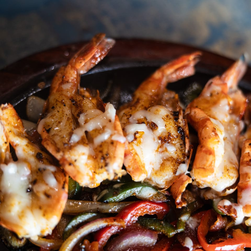 Sizzling shrimp fajitas with melted cheese, bell peppers, and onions in a hot skillet.