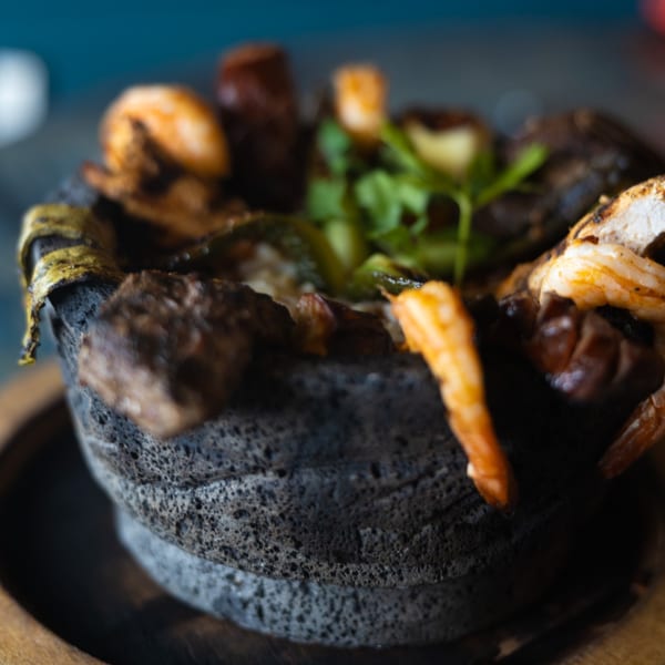 Molcajete dish from Pueblo Viejo Mexican Restaurant, filled with grilled shrimp, meat, and vegetables.