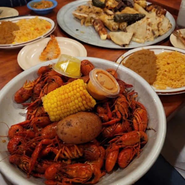A large bowl of crawfish, corn on the cob, and a potato, with other Mexican dishes.