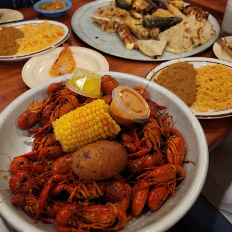 A large bowl of crawfish, corn on the cob, and a potato, with other Mexican dishes.