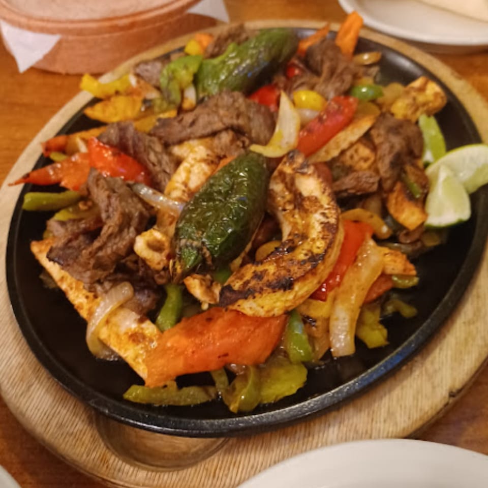 Sizzling fajitas with steak, chicken, colorful peppers, onions, and lime on a black skillet.