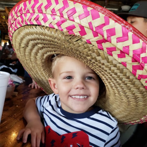 A smiling child wearing an oversized pink and straw sombrero at Pueblo Viejo Mexican Restaurant.