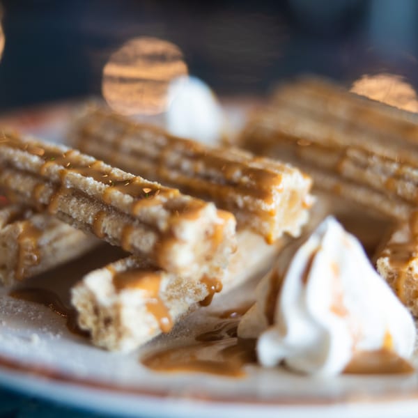Churros drizzled with caramel sauce and topped with whipped cream on a white plate.