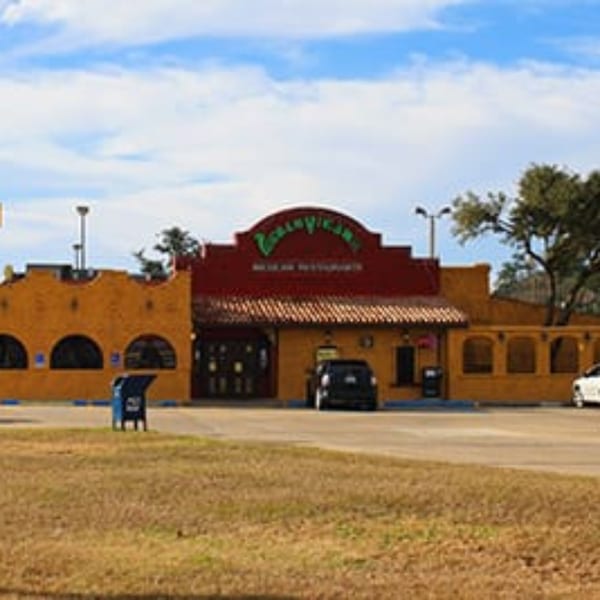 Exterior of Pueblo Viejo Mexican Restaurant, a yellow building with a red roof and sign, under a blue sky.