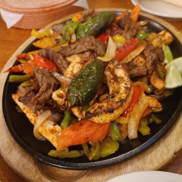 Sizzling Pueblo Viejo Mexican Restaurant fajitas with steak, chicken, peppers, and onions on a cast iron skillet.