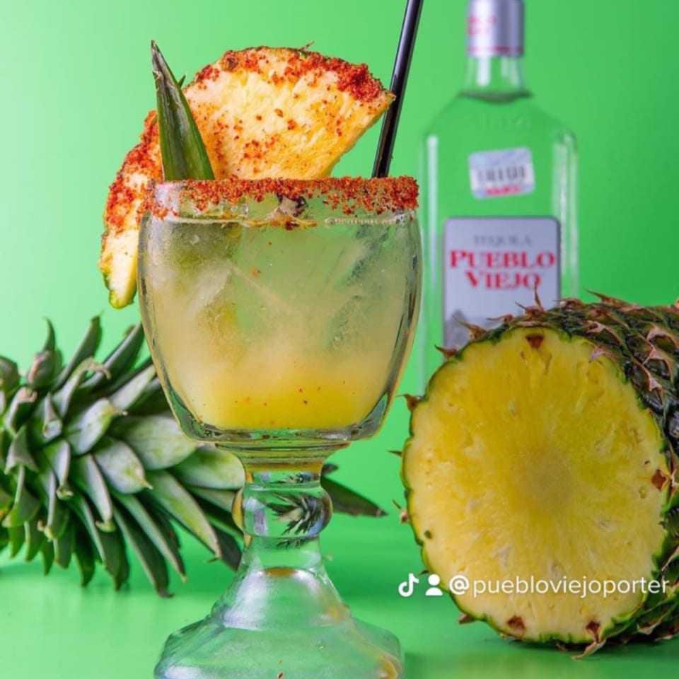 Pueblo Viejo Mexican Restaurant's pineapple margarita with chili-lime rim, pineapple slices, and tequila bottle.