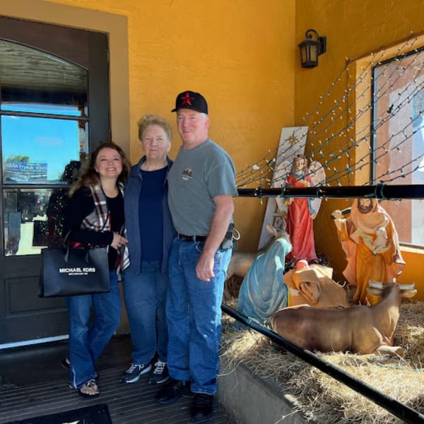 Three people posing next to a nativity scene with string lights outside Pueblo Viejo Mexican Restaurant.