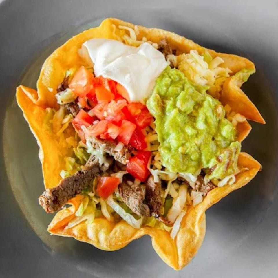 A taco salad in a crispy tortilla bowl, topped with meat, lettuce, tomatoes, sour cream, and guacamole.