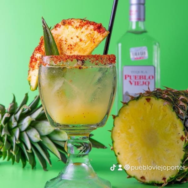 Pueblo Viejo pineapple margarita with chili-lime rim, pineapple slices, and a bottle of tequila.