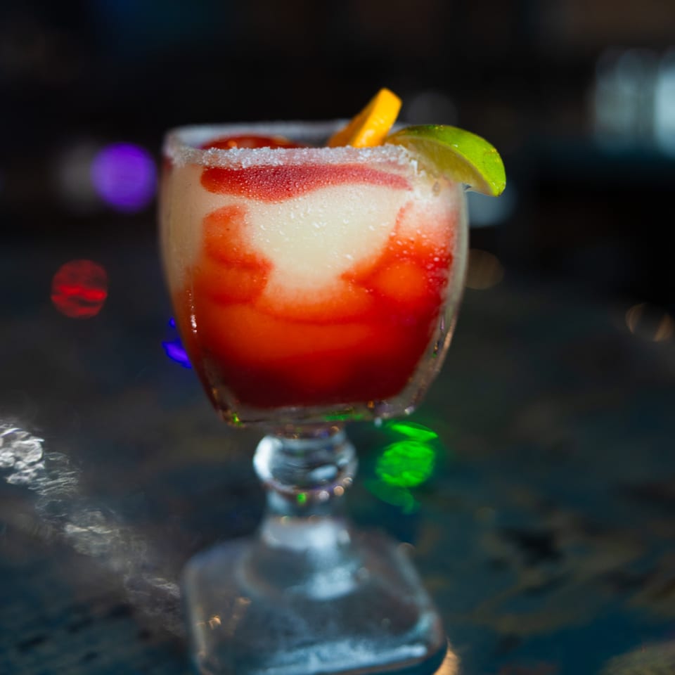 A vibrant strawberry and lime margarita with a salted rim, garnished with citrus slices.