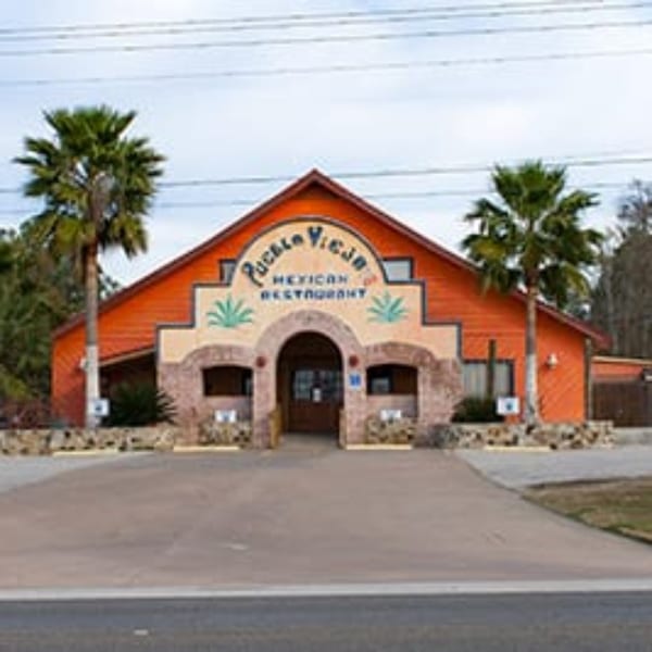 Pueblo Viejo Mexican Restaurant's orange building with a brown arched entrance and two palm trees.
